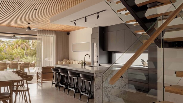 A modern kitchen with a marble island, bar stools, and a wooden staircase. - Maison by Khove (Broadbeach Waters)