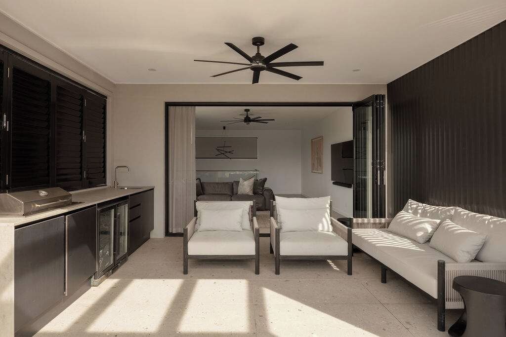 A modern living space with a sofa, chairs, a ceiling fan, and a kitchen area.