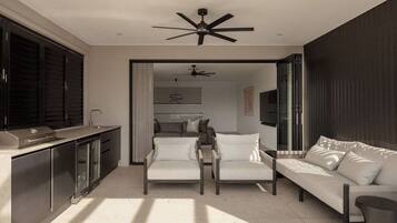A modern living space with a sofa, chairs, a ceiling fan, and a kitchen area.