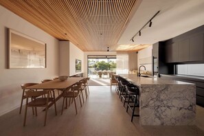 Una cocina moderna con una isla de mármol, techo de madera y un comedor con sillas y mesa.