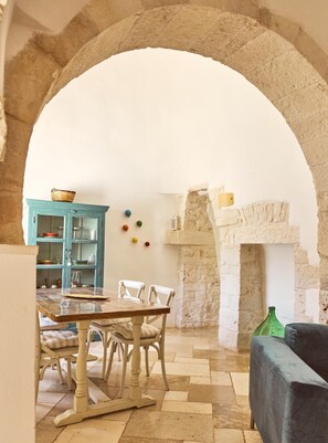 A rustic dining area with a stone archway, a wooden table, white chairs, a teal cabinet, and a fireplace. - Trulli with swimming pool in the heart of Itria Valley (Martina Franca)