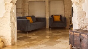 Ein Zimmer mit einem rundbogigen Steingewölbe, zwei dunklen Sofas mit gelben Kissen, einer Holztruhe und einem Fliesenboden.