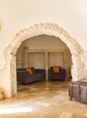 A room with an arched stone doorway, two dark sofas with yellow cushions, a wooden chest, and a tiled floor. - Trulli with swimming pool in the heart of Itria Valley (Martina Franca)