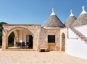 A stone building with a covered patio, stone steps, and a small table. - Trulli with swimming pool in the heart of Itria Valley (Martina Franca)