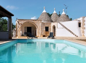 A pool with lounge chairs, a stone building with a staircase, and a clear sky. - Trulli with swimming pool in the heart of Itria Valley (Martina Franca)