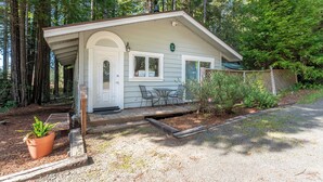 A small cabin with a porch, a table, and chairs, surrounded by trees. - Come live your magical cottage-core dreams at Green Tree Cottage in Mendocino! (Mendocino)