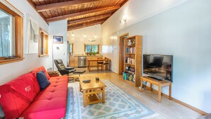 A living room with a red sofa, wooden coffee table, and a TV on a stand. - Come live your magical cottage-core dreams at Green Tree Cottage in Mendocino! (Mendocino)