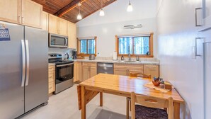 A modern kitchen with wooden cabinets, stainless steel appliances, and a wooden dining table. - Come live your magical cottage-core dreams at Green Tree Cottage in Mendocino! (Mendocino)