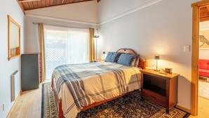 A bedroom with a bed, bedside tables, a nightstand, a lamp, a window with curtains, and a wooden ceiling. - Come live your magical cottage-core dreams at Green Tree Cottage in Mendocino! (Mendocino)