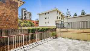 Un balcone con ringhiera in metallo, piante in vaso e vista sugli edifici circostanti.