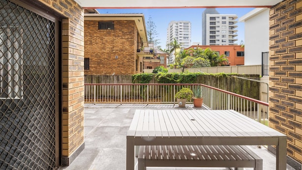 Un balcone con tavolo e sedie in legno, un recinto in metallo e vista sugli edifici circostanti.