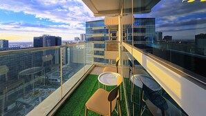 A modern balcony with a glass railing, a small seating area with chairs and a table, and a view of the cityscape.