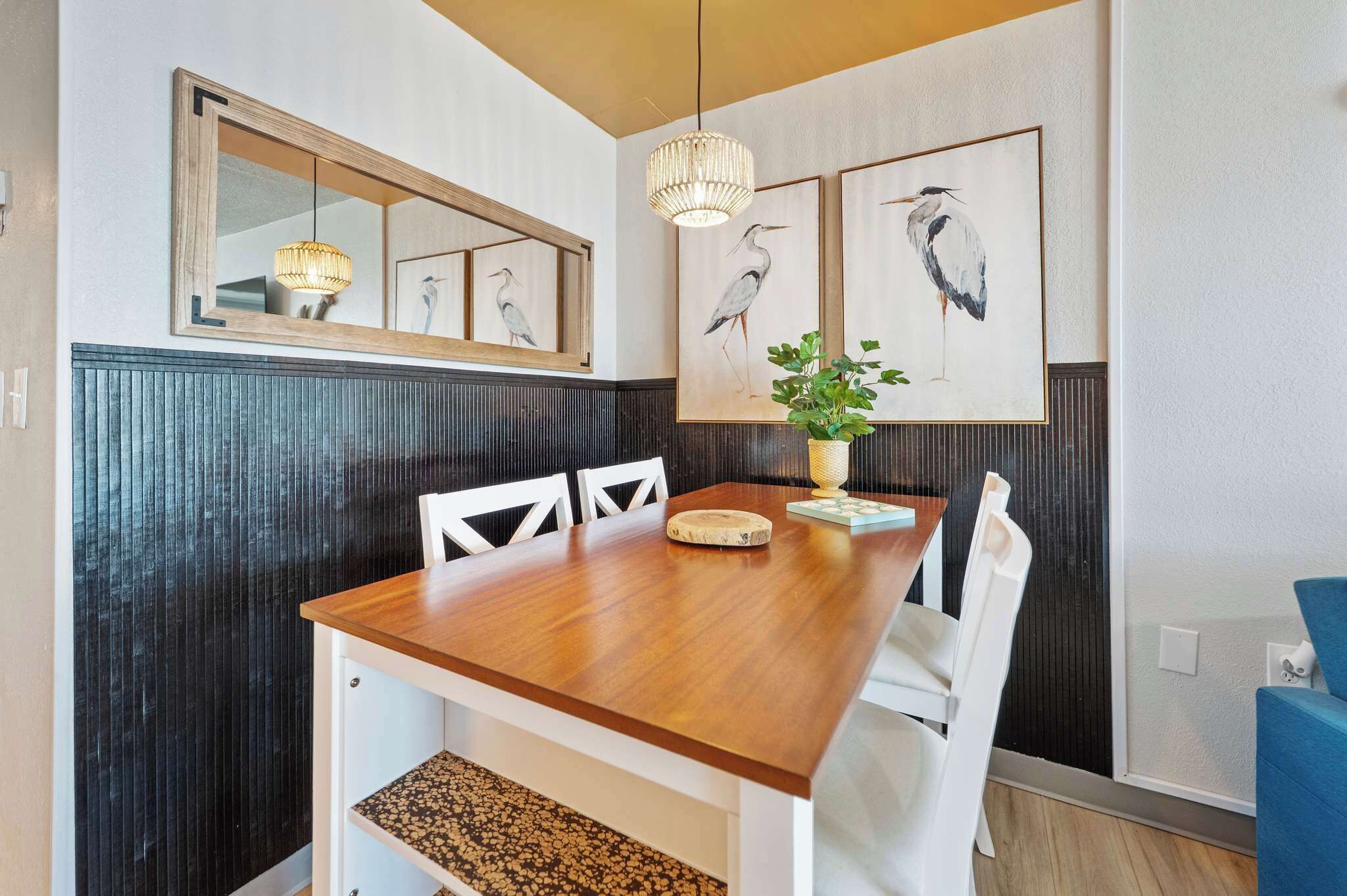A dining area with a wooden table, white chairs, a hanging light fixture, and wall-mounted artwork.