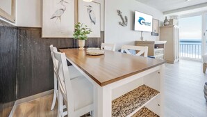 A dining area with a wooden table, white chairs, a potted plant, and artwork on the wall. - Amazing Large Private Studio Condo with Amazing View (Myrtle Beach)