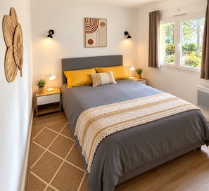 Une chambre à coucher comprenant un lit, deux tables de chevet, une lampe fixée au mur, une fenêtre avec des rideaux et un tapis à motifs géométriques.