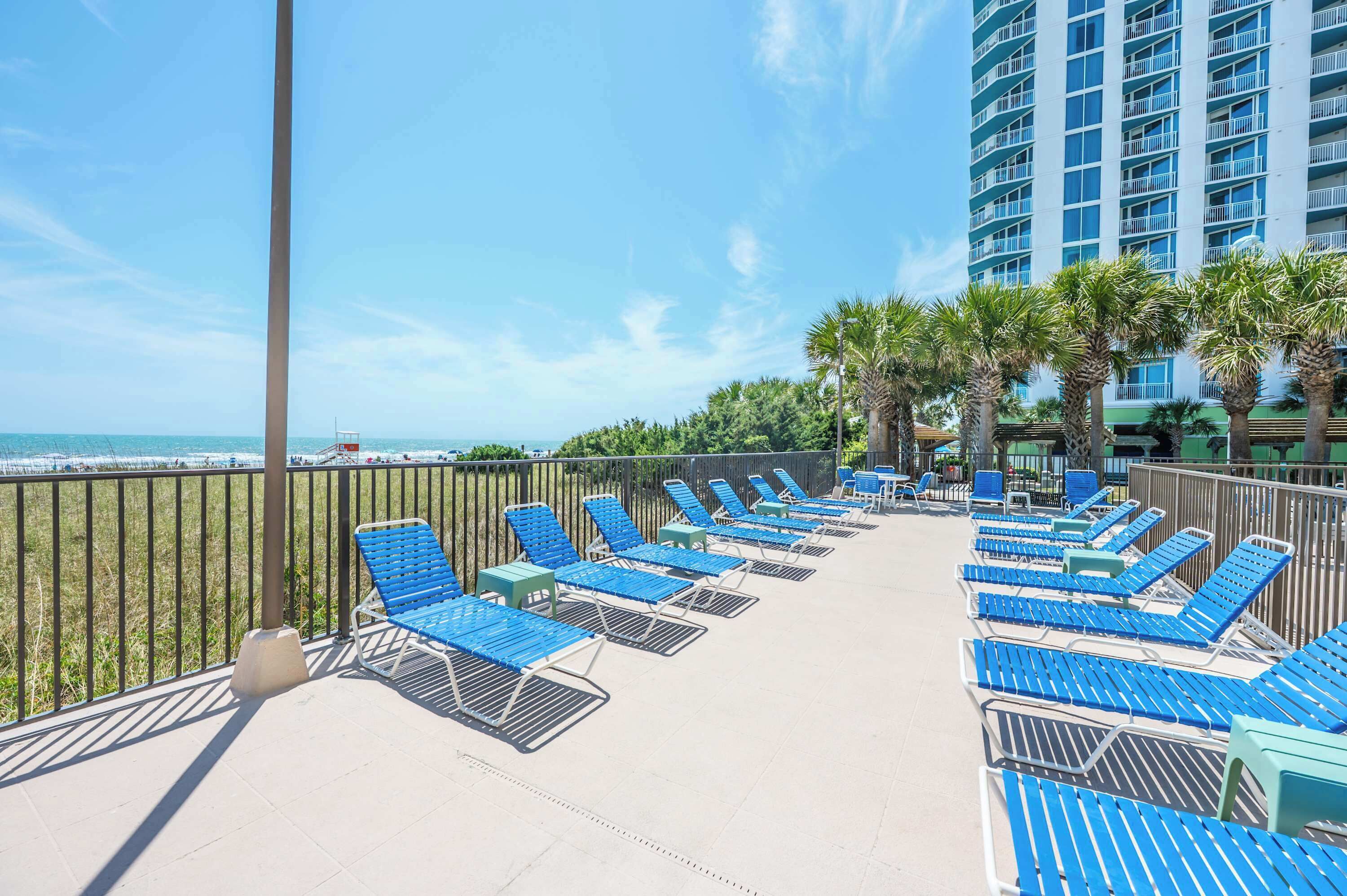 A balcony with blue lounge chairs, a view of the ocean, and a tall building in the background.
