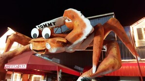 A large crab mascot with a sign that reads 'TOMMY' in front of a building with a sign that says 'GIANT CRAB.'