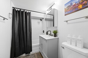 A modern bathroom with a shower curtain, a sink with a mirror, a plant, and toiletries on a shelf. - Spacious 5-bedroom house in charming Chicago on a quiet secluded block. (Chicago)