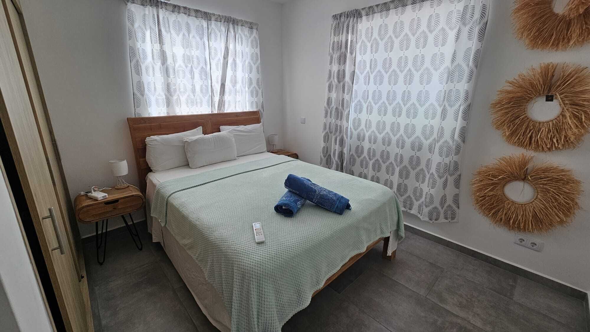 A bedroom with a bed, a nightstand, a lamp, and a wall with decorative wall hangings.