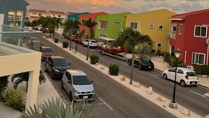 Een straatbeeld met kleurrijke gebouwen, geparkeerde auto's en een heldere lucht.