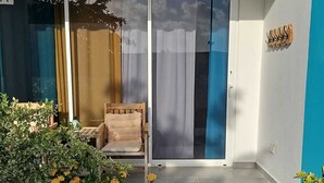 Een modern gebouw met een blauwe gevel, een glazen schuifdeur als ingang, een klein zitgedeelte met een bank en kussens, en een grindpad dat naar de ingang leidt.