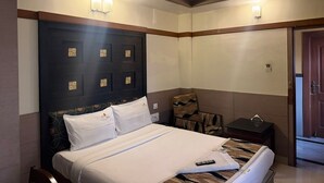 Habitació d'hotel amb un llit, una taula, una cadira, un ventilador de sostre i una porta.
