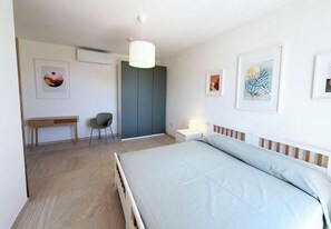 Ein Schlafzimmer mit einem Bett, einem Schreibtisch, einem Stuhl, einem Kleiderschrank und Wandbildern.