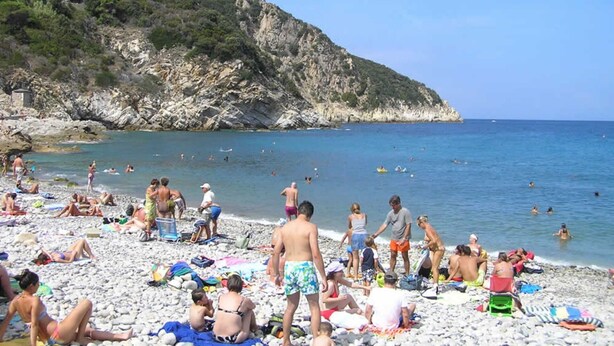 A crowded beach with people sunbathing and swimming, rocky cliffs in the background, and clear blue water. - Casa Comandante – Two-Level Apartment with Sea View in Marciana (Marciana)