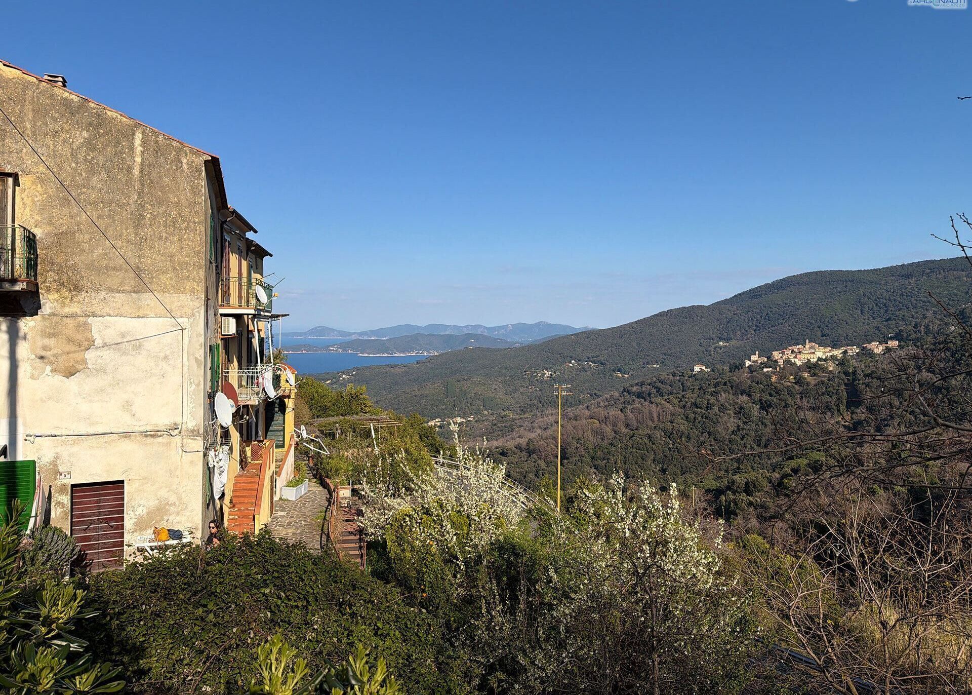 A hillside building with a balcony overlooking a valley and distant mountains.
