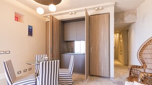 A modern dining area with striped chairs and a glass table, adjacent to a kitchen with wooden cabinets and a built-in oven. - VILLA RITTER ORIZZONTE (Marina di Campo)
