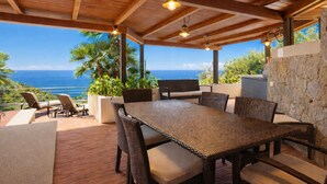 A covered outdoor dining area with a view of the ocean, wooden ceiling beams, and wicker furniture. - VILLA RITTER ORIZZONTE (Marina di Campo)