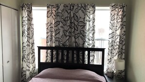Une chambre à coucher avec un lit, une table de chevet, une lampe et des rideaux à motifs de feuilles.