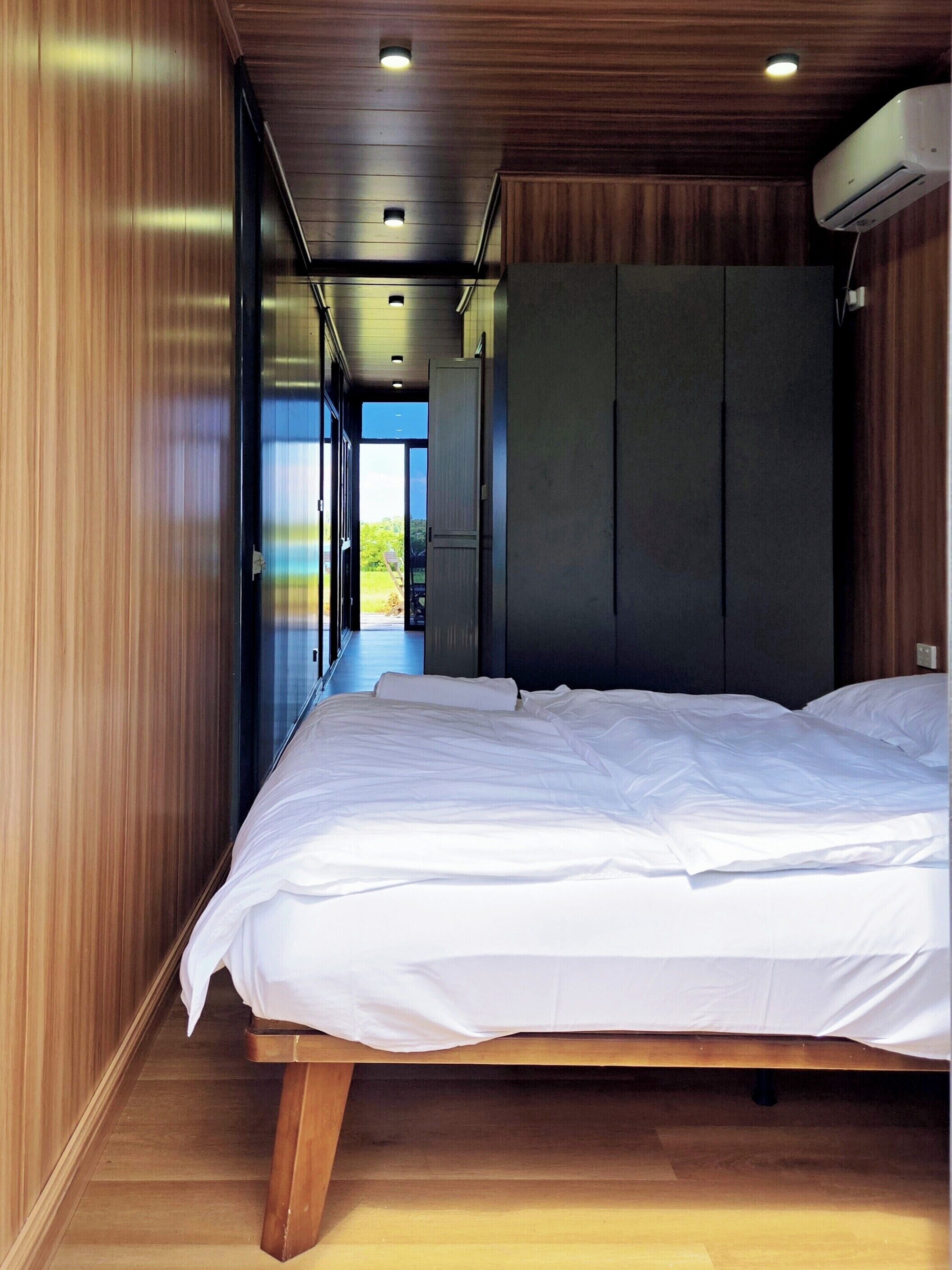 A bedroom with a bed, wooden walls, and a view through an open door.