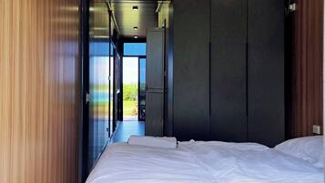 A bedroom with a bed, wooden walls, and a view through an open door.
