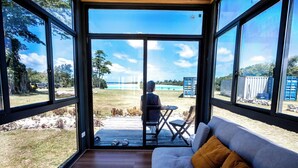 A room with large windows, a wooden floor, and a grey sofa with a brown pillow. - Nawesa Resort (Rentapow)