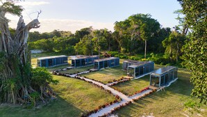 A row of modern, blue modular buildings with solar panels, surrounded by lush greenery and a large tree. - Nawesa Resort (Rentapow)