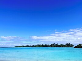 Cielo azul despejado y mar turquesa tranquilo con una isla distante cubierta de árboles.