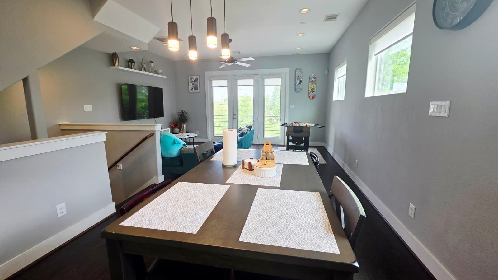 A modern dining area with a long table, chairs, and a ceiling fan.