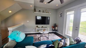 Ein modernes Wohnzimmer mit einem türkisblauen Sofa, einem Couchtisch, einem flachbildfernseher an der Wand und einer kleinen weißen Regal mit Dekorationselementen.