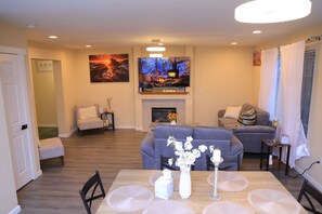 A living room with a fireplace, a sofa, a television, and a dining table with placemats. - Wonderful Entire home in Kent 3-bedroom with AC in cool walk in train station (Kent)