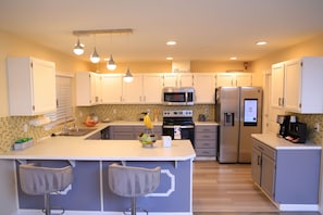 A modern kitchen with white cabinets, stainless steel appliances, and a central island with bar stools. - Wonderful Entire home in Kent 3-bedroom with AC in cool walk in train station (Kent)