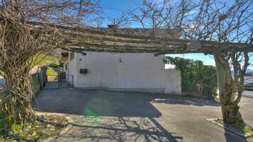 A covered outdoor area with a concrete floor, a pergola, and a white building with a door.