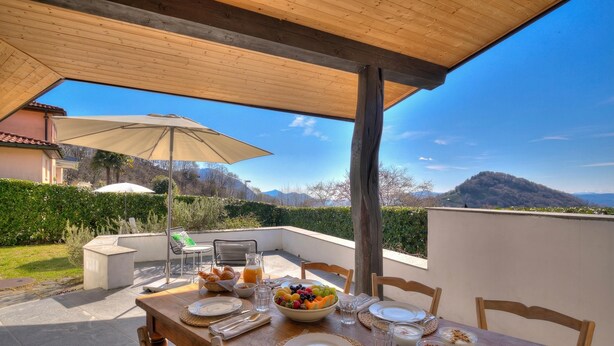 An outdoor dining area with a table set for breakfast, a wooden pergola overhead, and a scenic mountain view in the background. - La Ca Da Bre - Garden House With Views (Lugano)