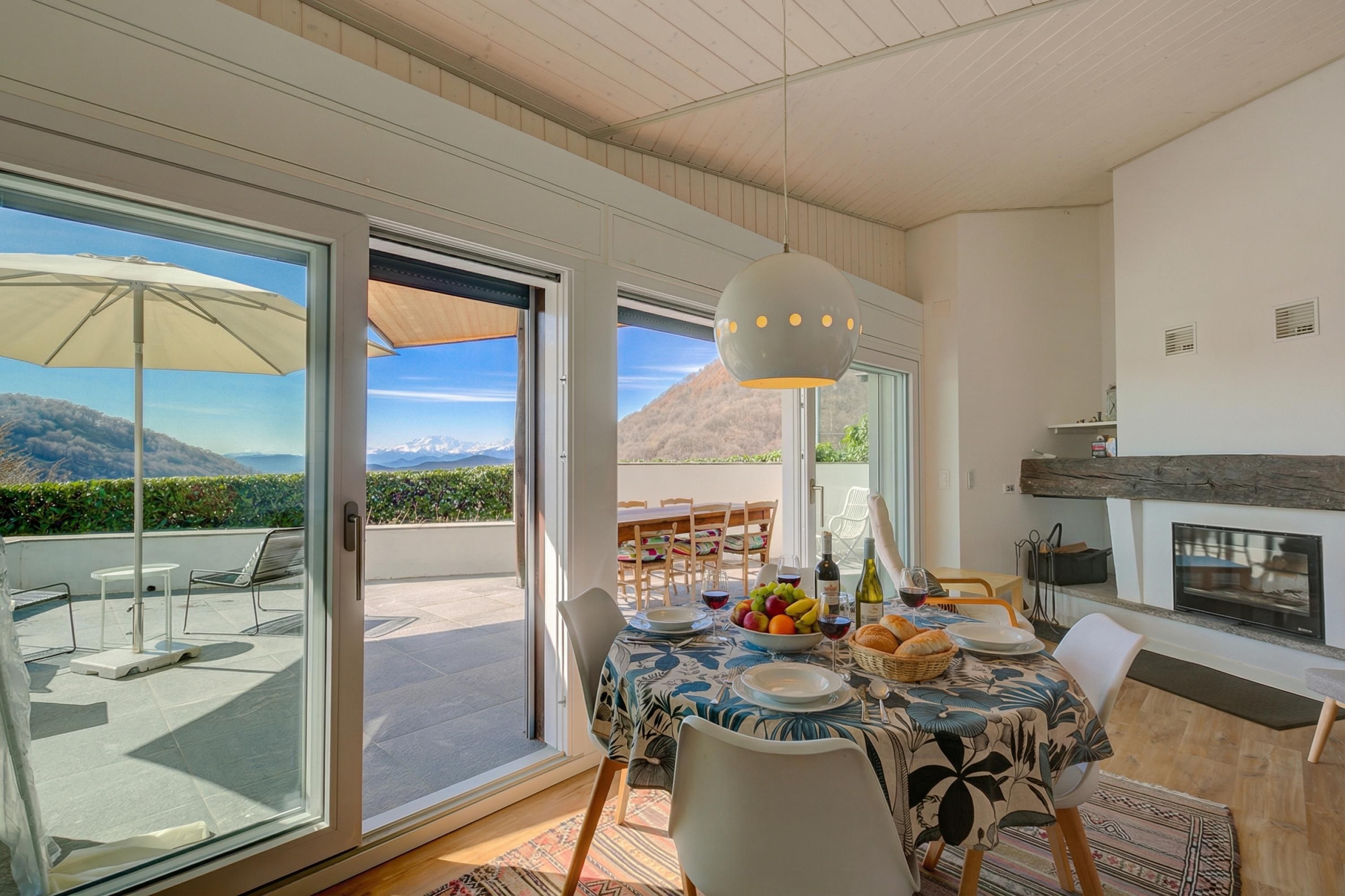 Un coin repas avec une table dressée pour deux personnes, une cheminée et une vue sur les montagnes, visible à travers de grandes portes coulissantes.