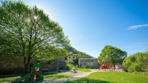 Un parque con juegos infantiles, un muro de piedra y un edificio al fondo.