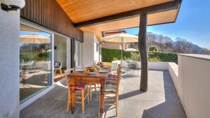 A covered patio with a wooden table and chairs, a glass door leading to an indoor area, and a view of the outdoors. - La Ca Da Bre - Garden House With Views (Lugano)