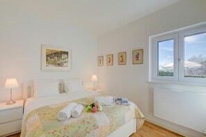 Ein ordentlich bezogenes Bett mit Blumendekor, eine Nachttischlampe und ein gerahmtes Bild an der Wand.