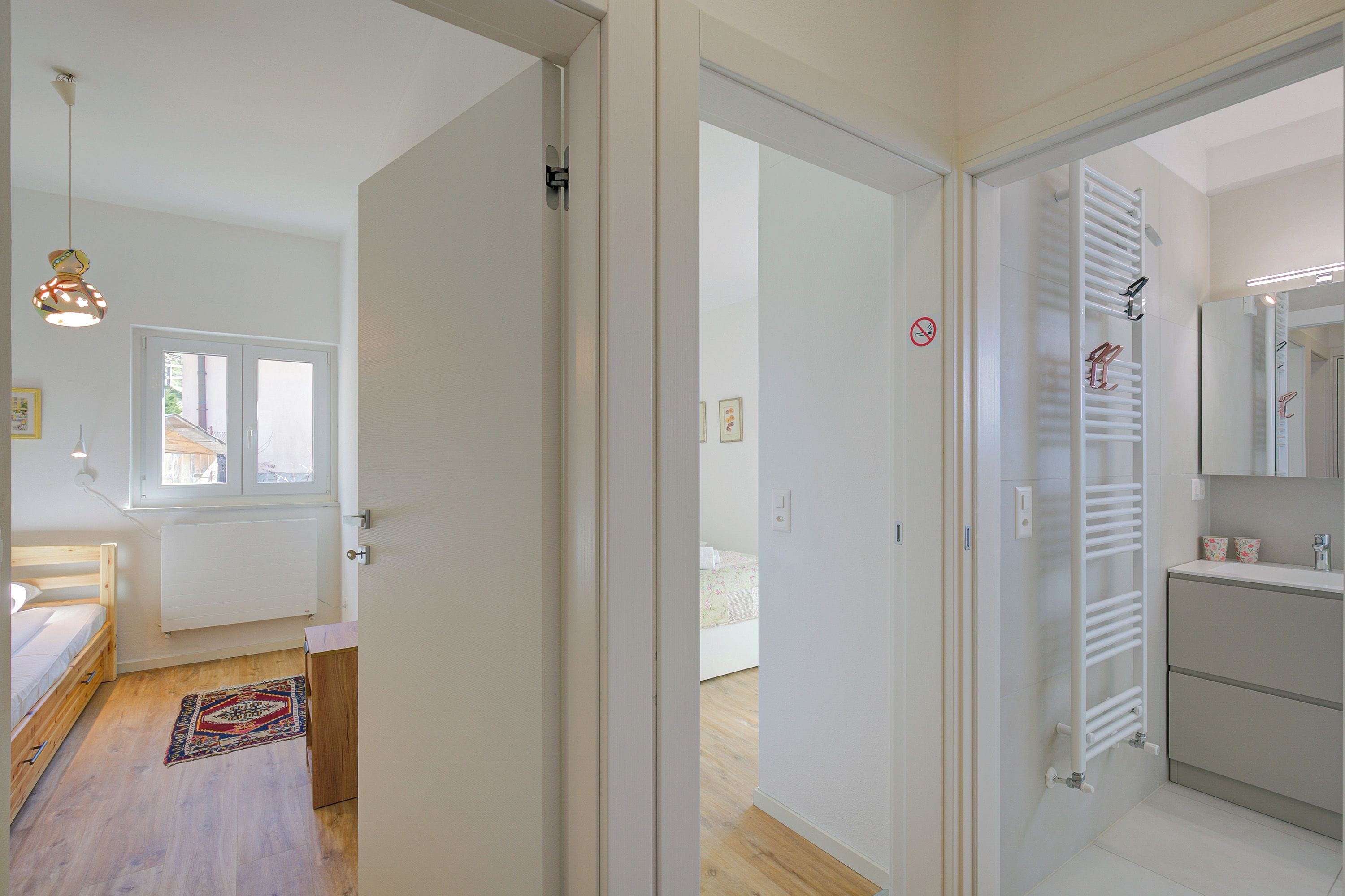 A room with a bed, a radiator, a window, and a door leading to another room.