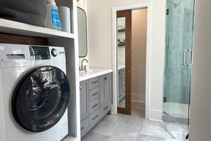 A compact bathroom with a front-loading washing machine, a sink, and a glass shower enclosure. - World Cup 5BR Sleeps 14 Pet Friendly Near KC Current + 10 Min to FIFA/ARROWHEAD (Kansas City)