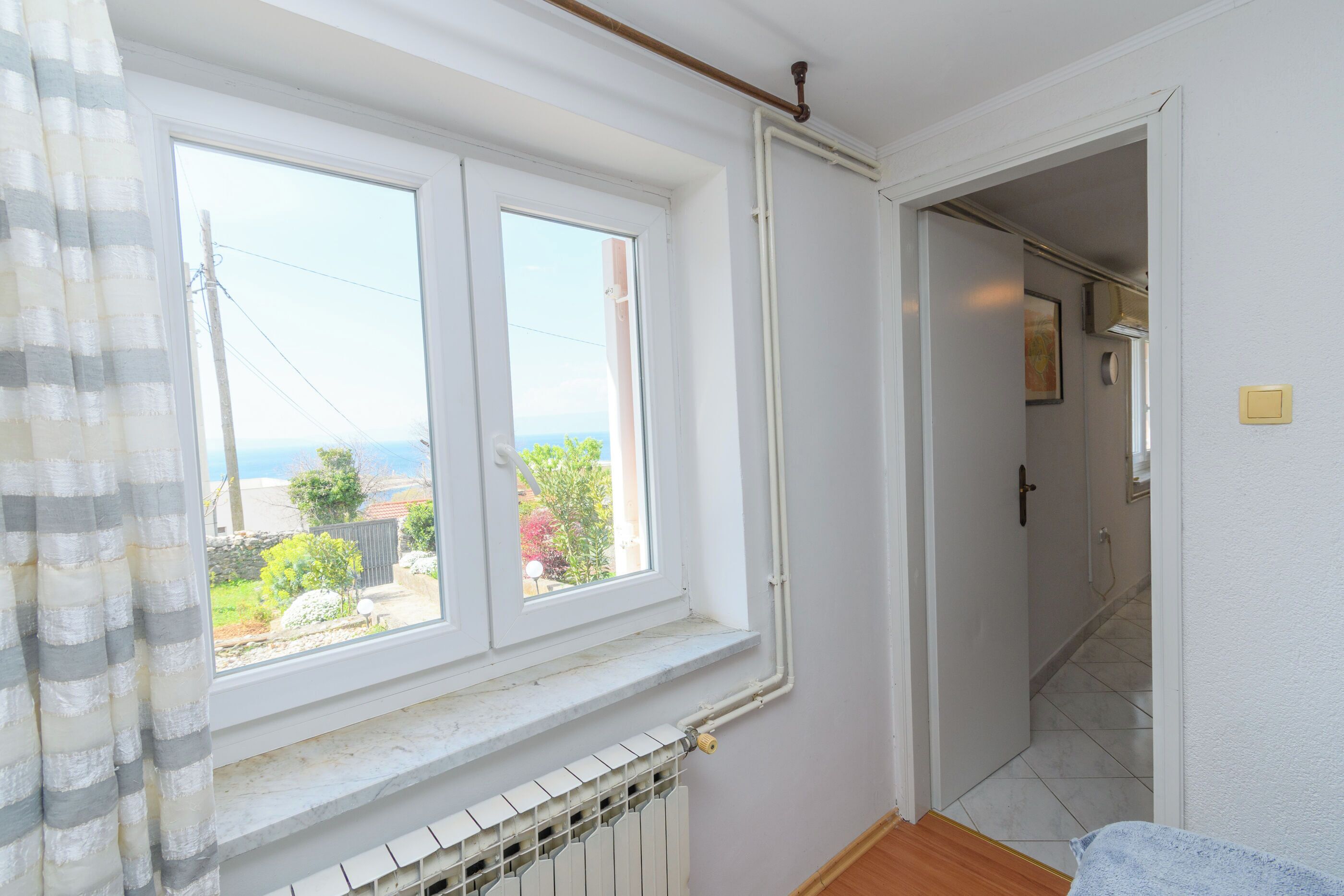 Een kamer met een raam, een radiator en een deur naar een andere kamer.